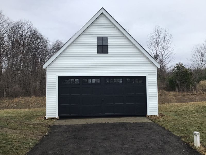 Black raised-panel double garage door with window inserts on a white two-story garage