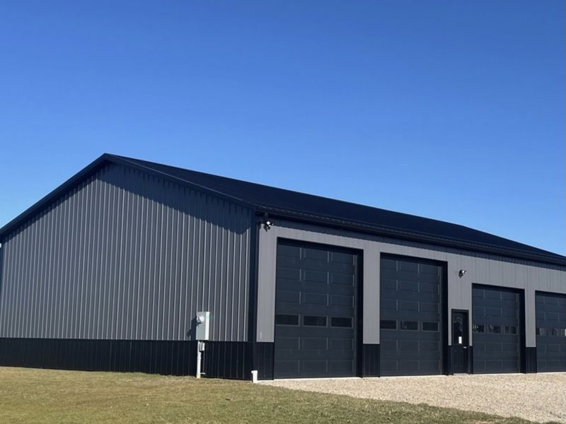 Four matching black garage doors on a dark steel shop building