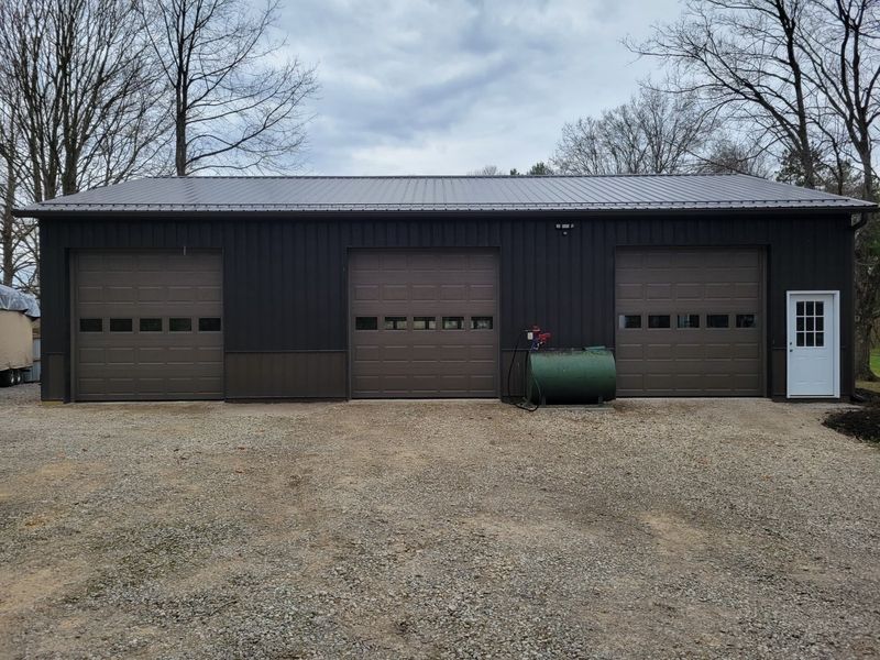 Three brown garage doors with window inserts on a dark brown pole barn