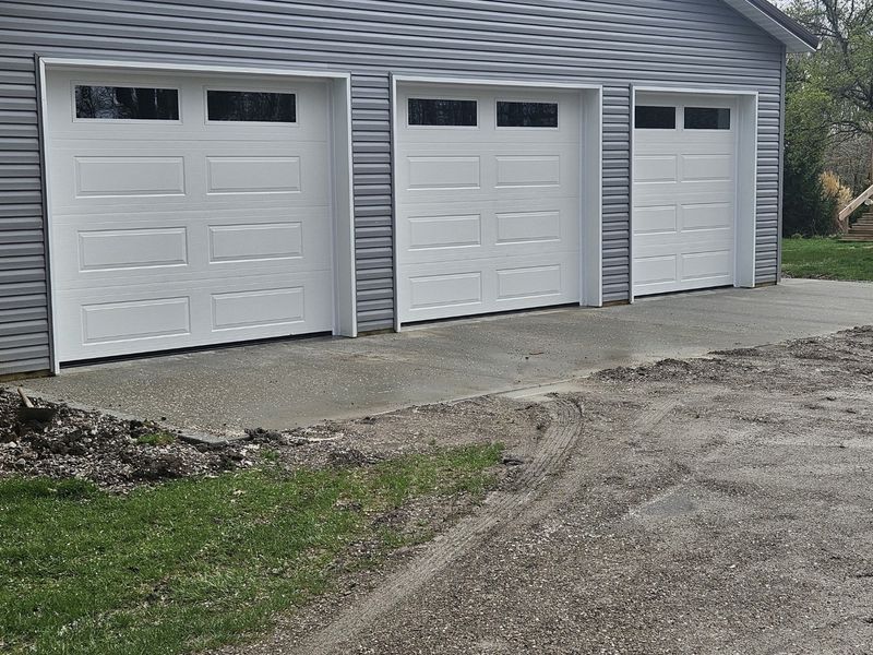 Three white long-panel garage doors on a gray pole barn, seen from the side