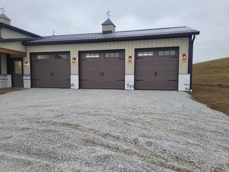 Three brown carriage-style garage doors with windows and coach lights on a new barndominium