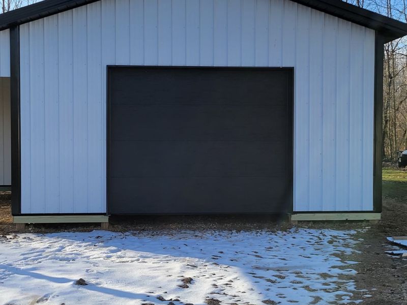 Black insulated garage door on a white pole barn in winter