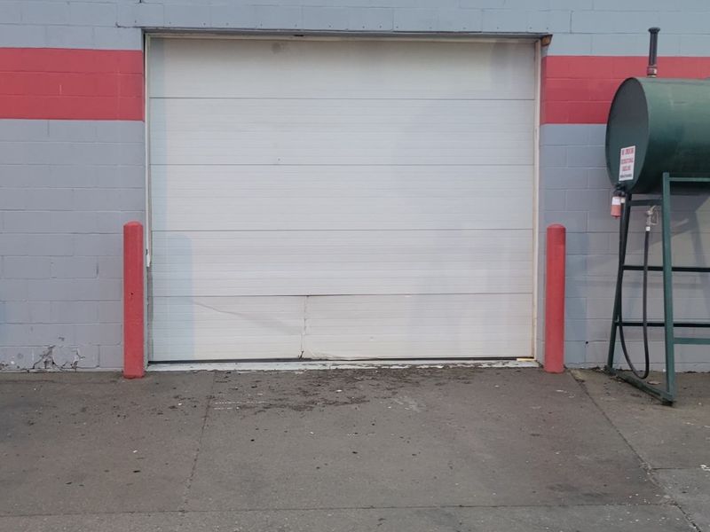 Damaged white commercial garage door on a block storefront before replacement