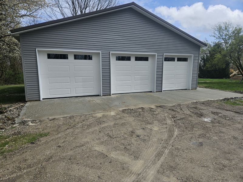 Three-car pole barn with white long-panel garage doors and a new concrete apron