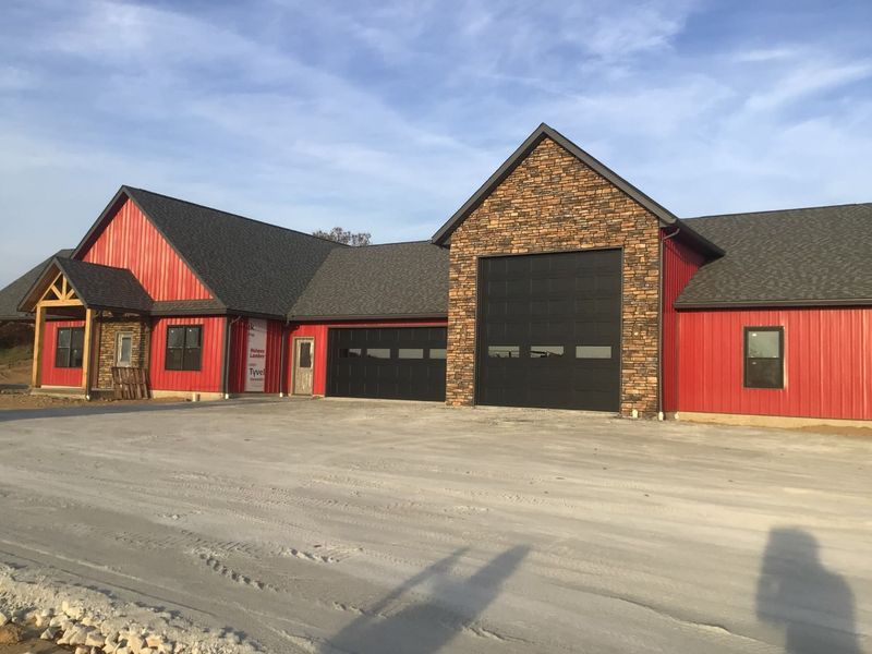 Tall black RV door and matching garage doors on a red barndominium with a stone gable